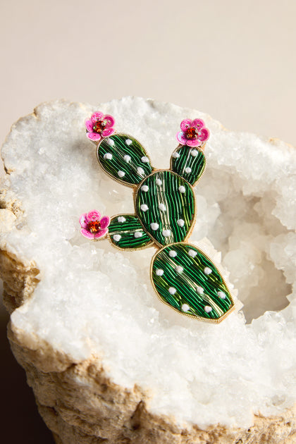 This vibrant Cactus Brooch showcases green segments adorned with white dots and pink flower accents, all set in a dazzling white crystal geode, offering a playful pop of color.