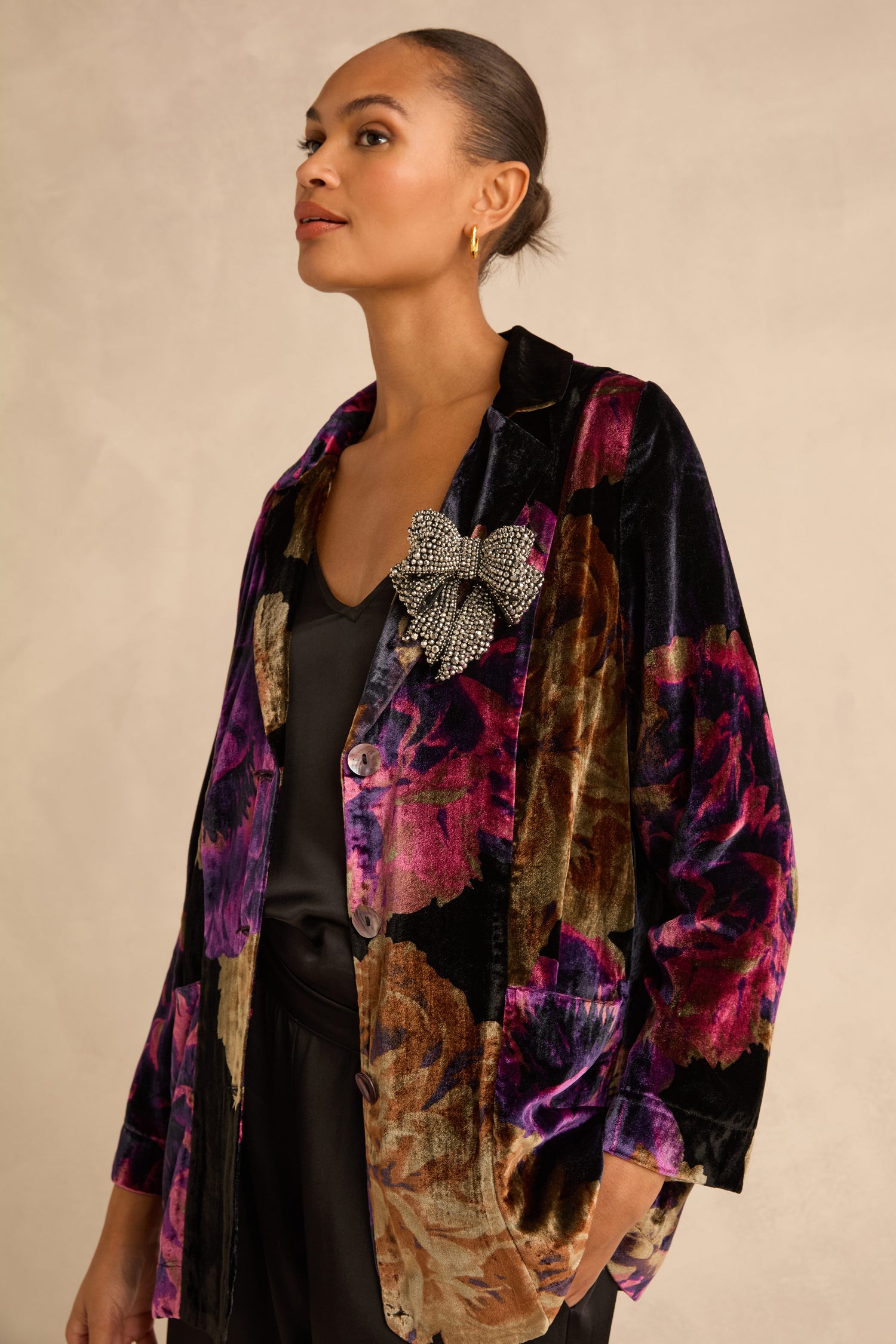 A large, silver-toned Silver Hand Beaded Bow Brooch pinned to the lapel of a floral velvet blazer.