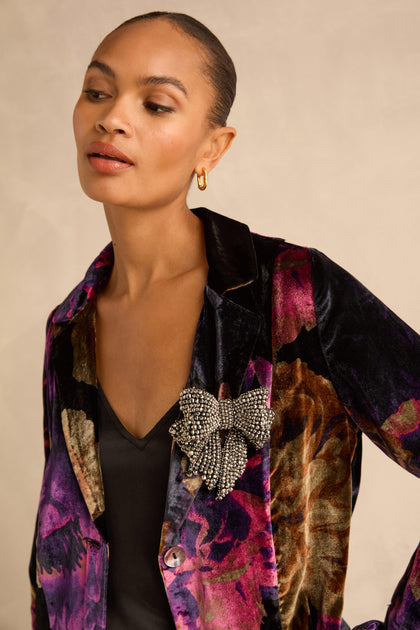 A Silver Hand Beaded Bow Brooch pinned to the lapel of a dark floral velvet blazer.