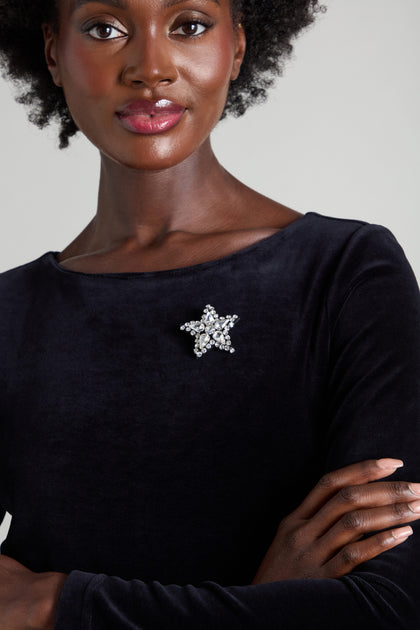 A person wearing a black top accessorized with the Star Brooch, which is embellished with rhinestones in the shape of a silver star.