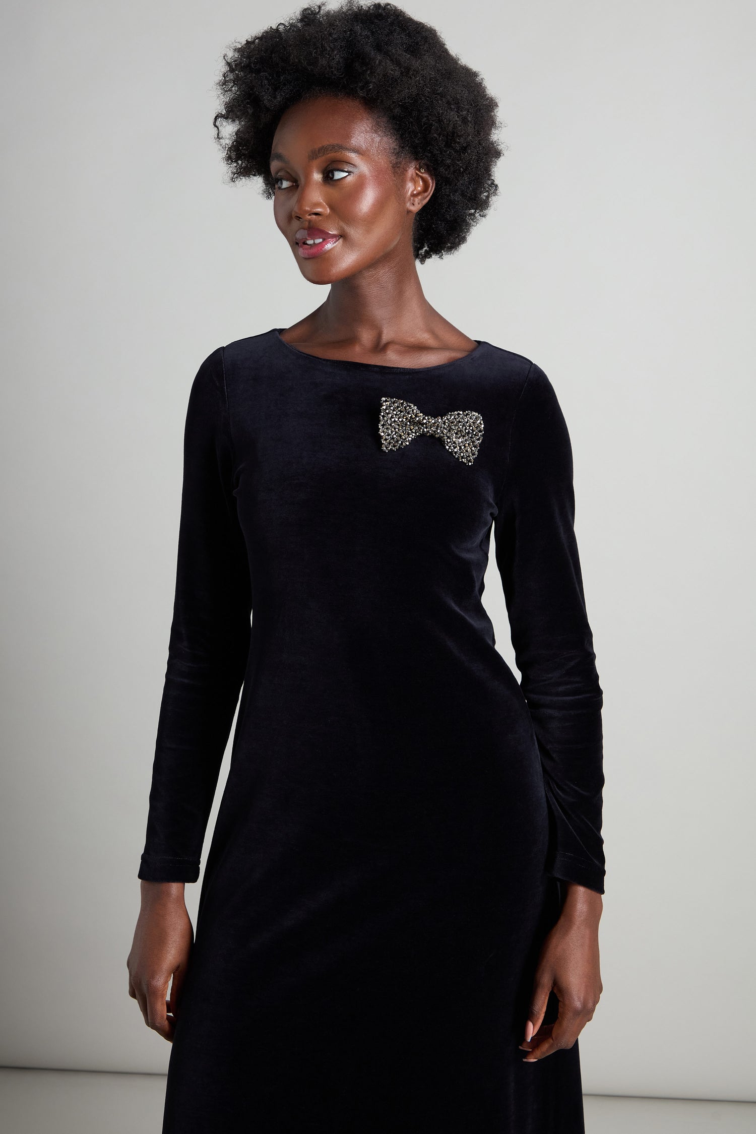 A woman adorned in a sophisticated long-sleeved black velvet dress that exudes an elegant shimmer, complemented by a leopard print Bow Tie Brooch.