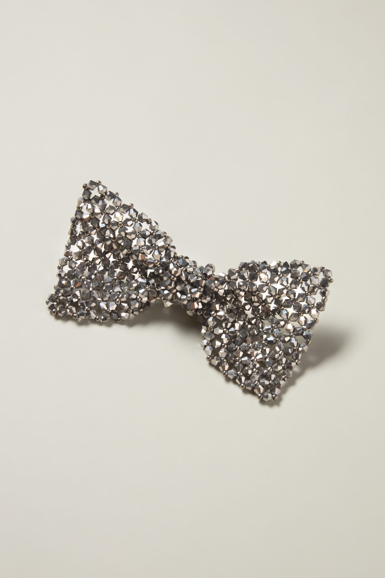 A Bow Tie Brooch featuring sparkling silver rhinestones is showcased on a plain off-white background, emitting an elegant shimmer.