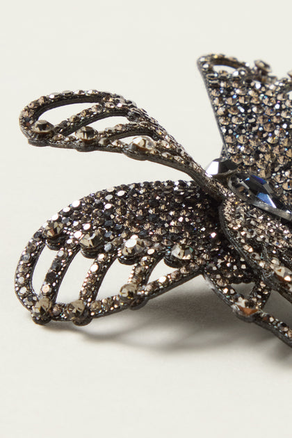 Close-up of the Crystal Butterfly Brooch, a decorative dark crystal accessory encrusted with rhinestones, shown against a plain light background.