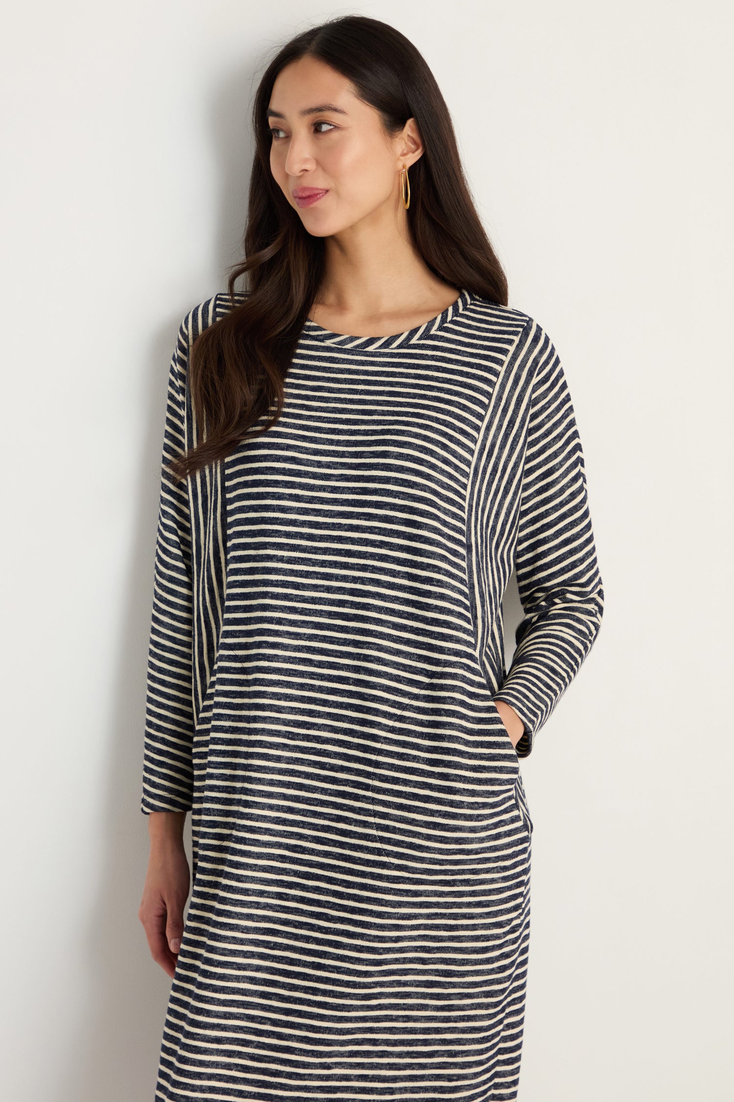 A woman with long dark hair wears the Textured Stripe Jersey Dress, featuring a relaxed fit and black and white textured stripes, while standing against a plain light-colored wall.