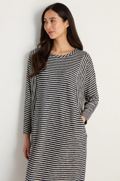 A woman with long dark hair wears the Textured Stripe Jersey Dress, featuring a relaxed fit and black and white textured stripes, while standing against a plain light-colored wall.