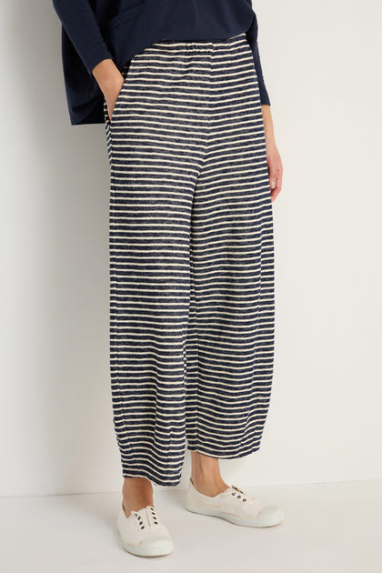 Wearing Textured Stripe Jersey Bubble Trouser in navy and white with an elasticated waist, styled with white sneakers, standing by a plain light wall.