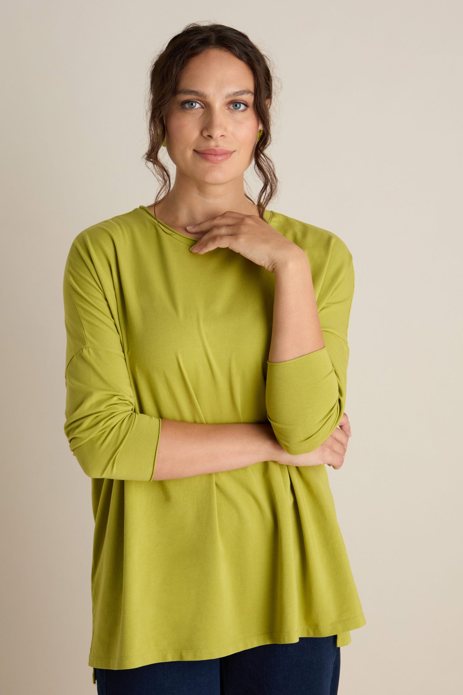 A person wearing the Cotton Jersey Relaxed Top in green stands with a relaxed body, touching their chin and looking directly at the camera against a plain background, capturing the essence of the Autumn season.