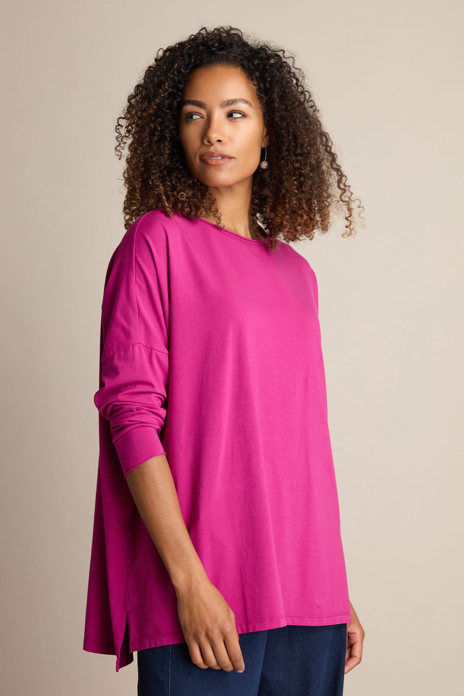 A woman wearing a Cotton Jersey Relaxed Top in soft magenta stands against a neutral background, looking to the side.