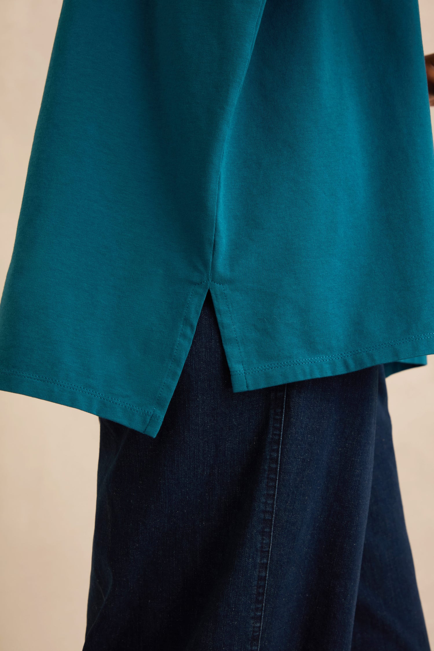 A close-up of the Cotton Jersey Relaxed Top in teal, featuring a boxy silhouette and a slit at the hem, styled over dark blue jeans.