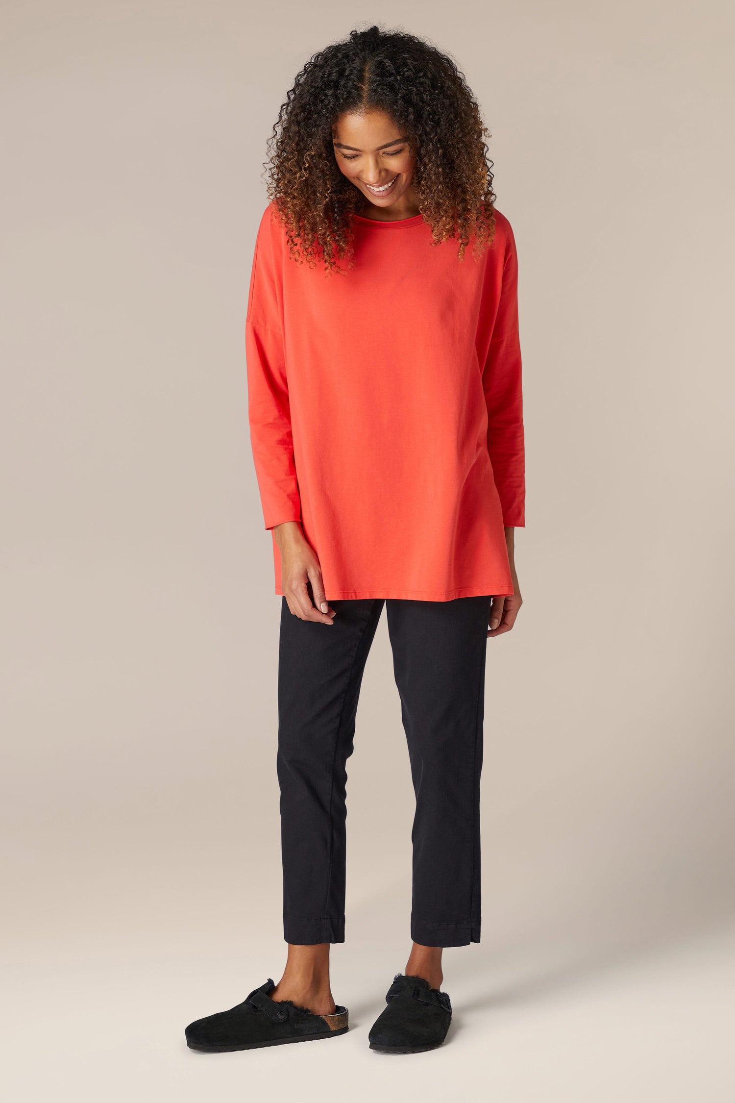 A woman in a cozy orange sweater and black pants, rocking a comfortable and relaxed Cotton Jersey Relaxed Top from her wardrobe.