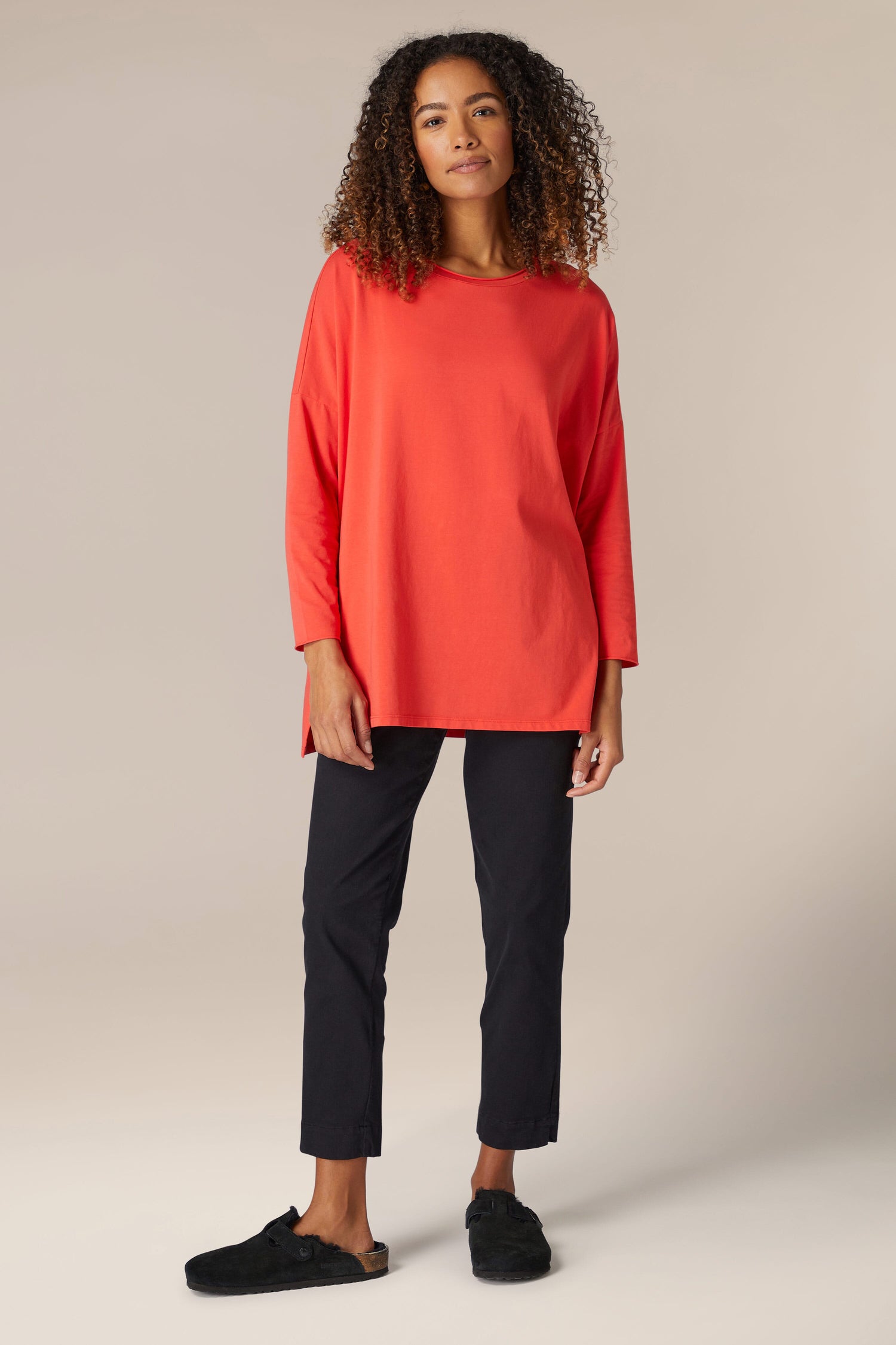 A woman wearing a comfortable orange sweater in the Cotton Jersey Relaxed Top and black pants.