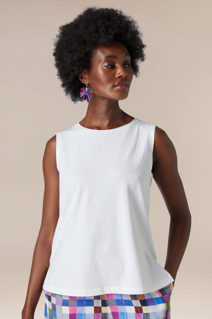 A woman with a natural afro hairstyle wearing a white Cotton Jersey Boxy Vest and a colorful skirt.