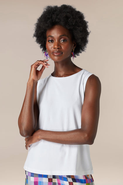 A woman with an afro wearing a white Cotton Jersey Boxy Vest and multicolored skirt, posing with one hand on her chin.