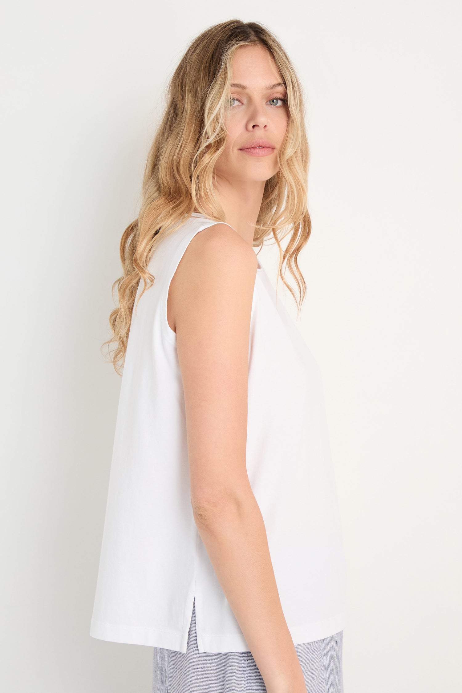 Woman with long, wavy blonde hair wearing the Cotton Jersey Boxy Vest in white and light-colored pants, standing sideways against a plain light background.