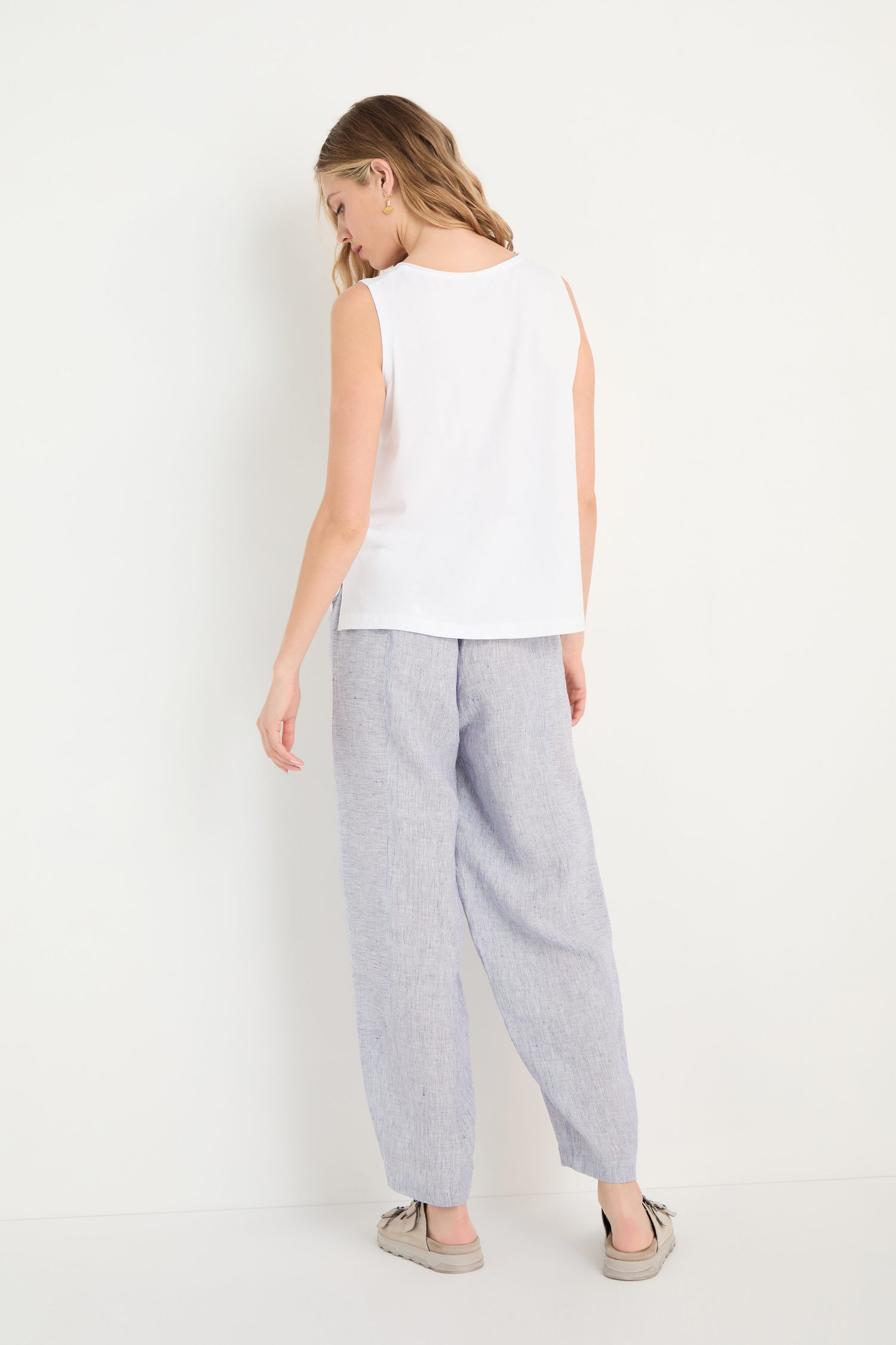 A woman stands facing away, wearing the Cotton Jersey Boxy Vest with loose light gray pants and beige shoes against a plain white background.