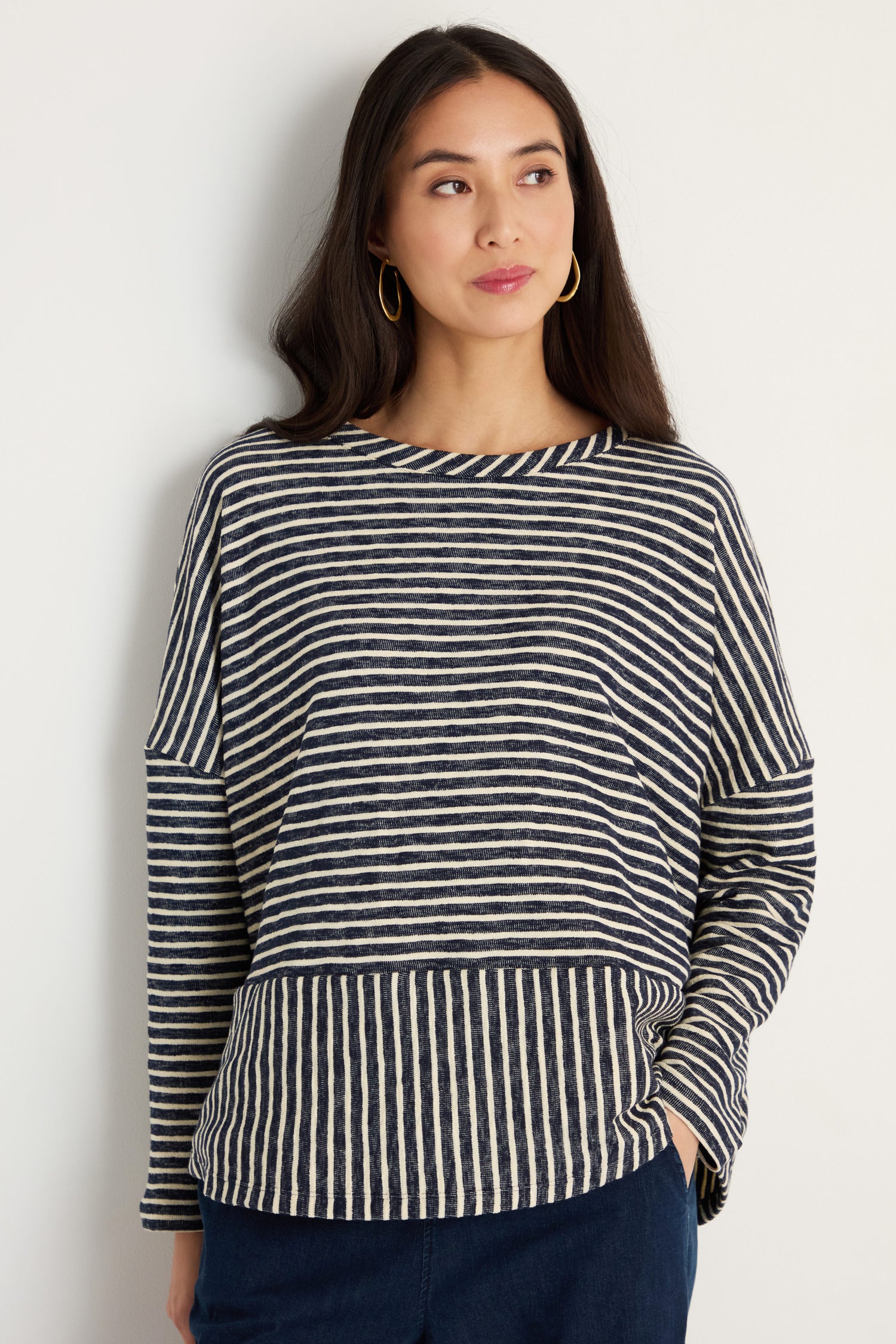 A woman with long dark hair is wearing the Textured Stripe Jersey Boxy Top in navy and white with dark pants, standing against a plain light-colored wall.