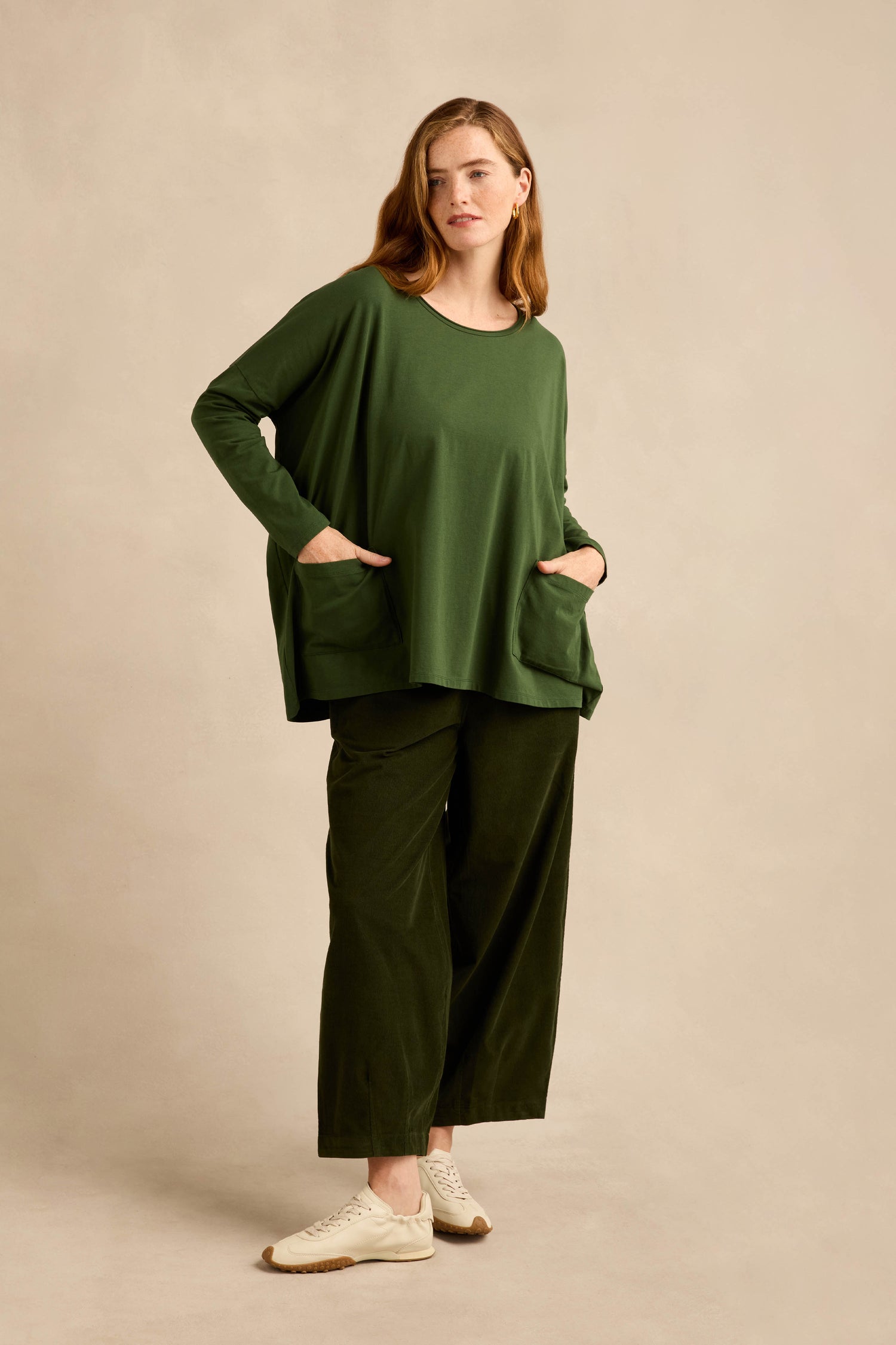 Person standing in a studio, wearing the Forest Cotton Jersey Pocket Top in loose green cotton jersey with wide-leg green pants and white sneakers.