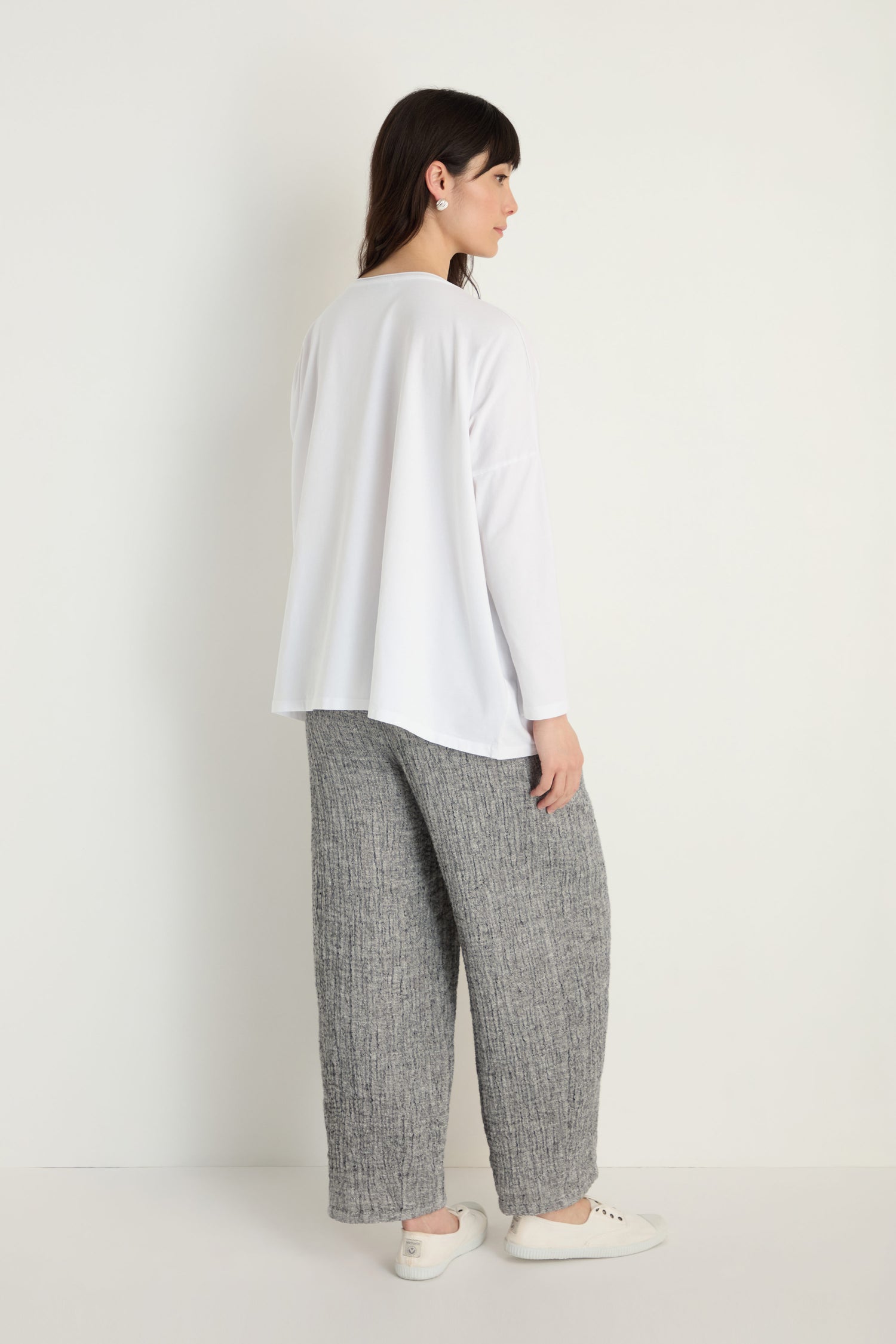 A person stands against a plain white background, facing away, wearing the Cotton Jersey Boxy Pocket Top with gray wide-leg pants and white slip-on shoes.