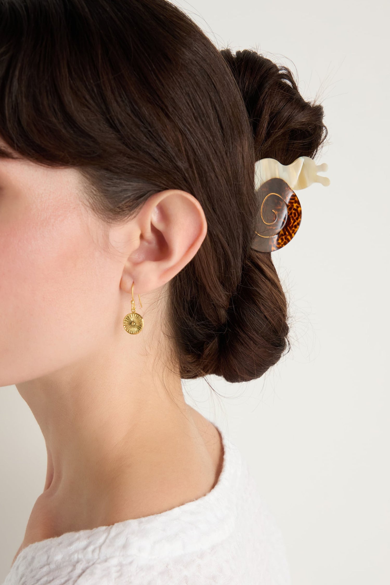 Close-up of a woman's head turned to the side, featuring a twisted updo secured with a Hand-painted Snail Hair Clip and gold round pendant earrings.