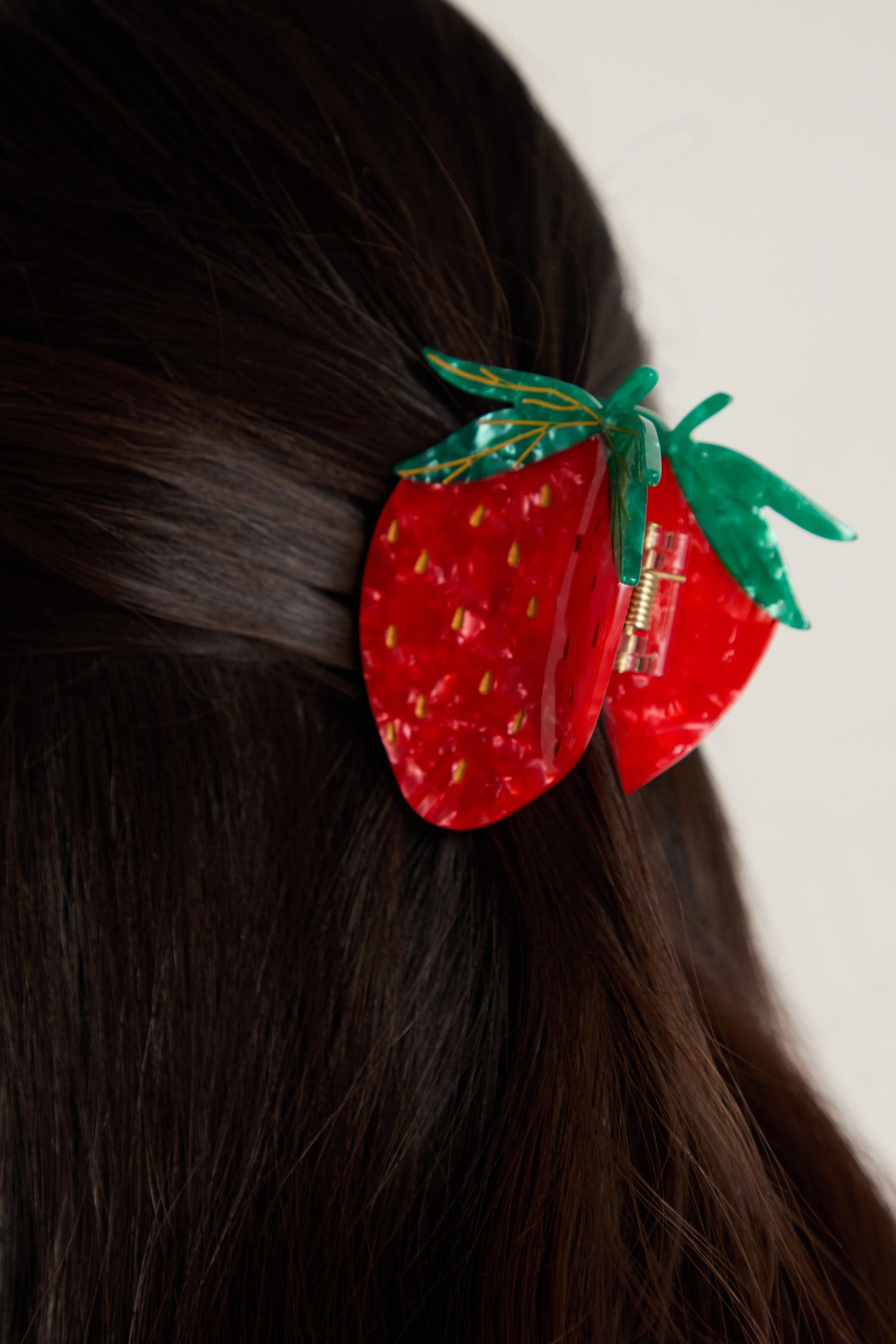 A person with dark hair wears the Hand Painted Strawberry Hair Clip, an eco-friendly accessory adorned with green leaves.