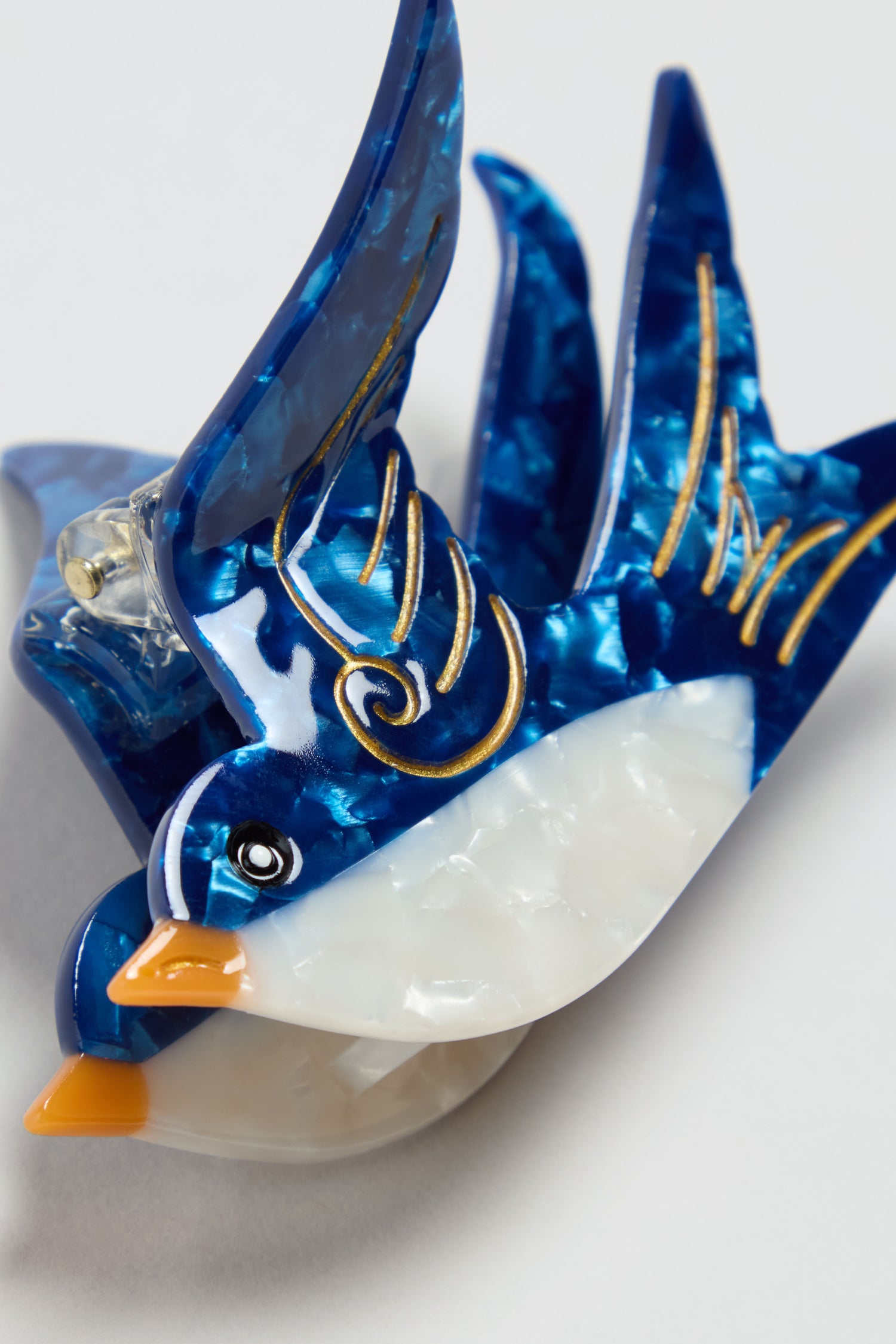 A close-up of the Hand-Painted Swallow Hair Clip, a bird-shaped accessory in blue and white with gold accents, crafted from glossy marbled material.