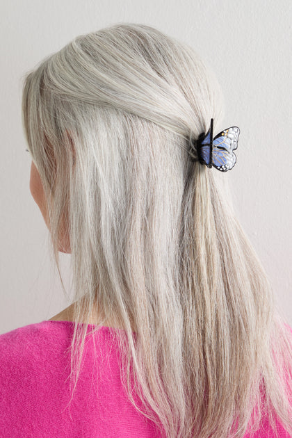 A person with long, straight gray hair, wearing a pink top, has a Hand-Painted Mini Monarch Butterfly Hair Clip securing part of their hair at the back.
