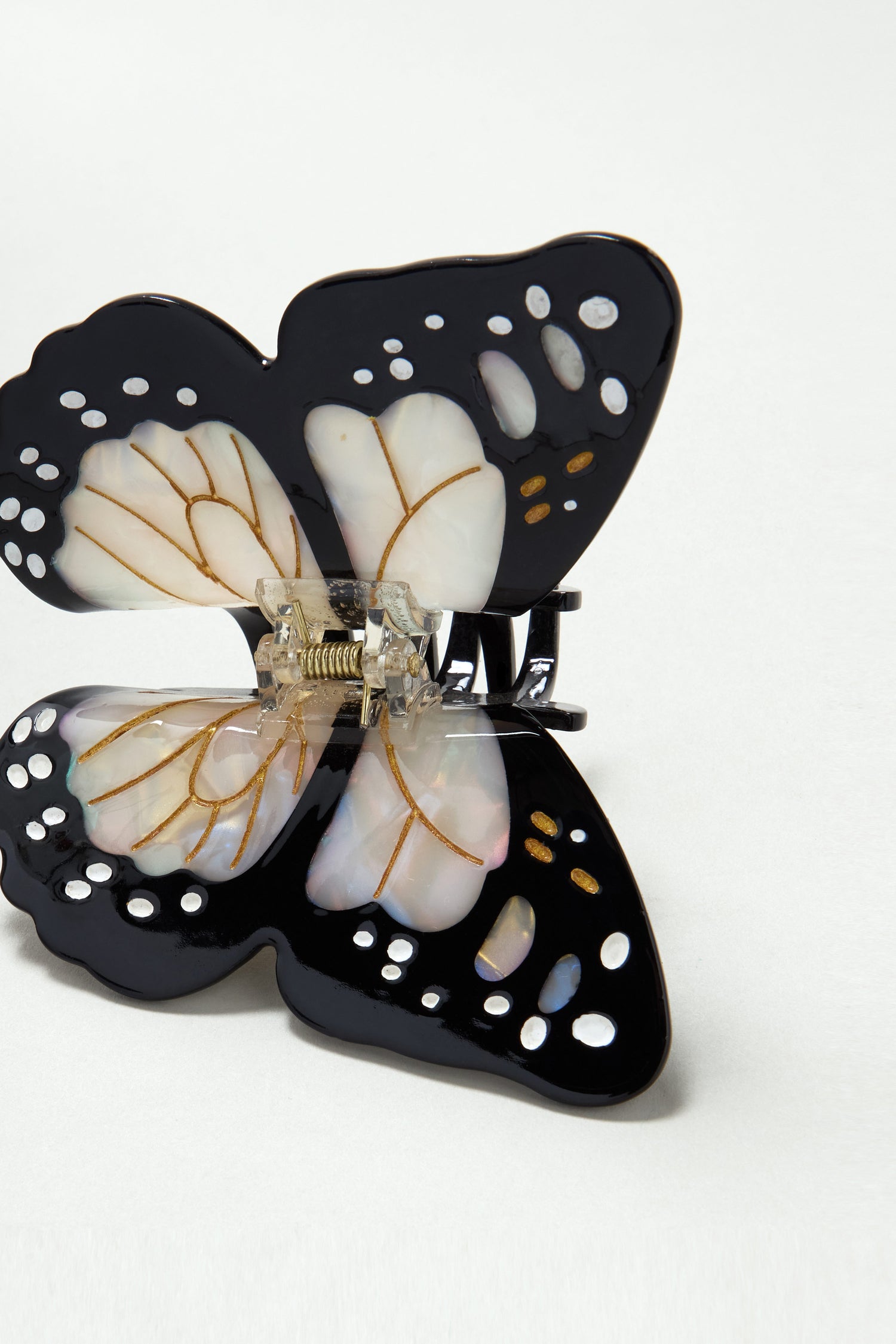 The Hand Painted Monarch Butterfly Hair Clip features black wings with white and gold accents and a metal spring hinge, shown on a plain white background.