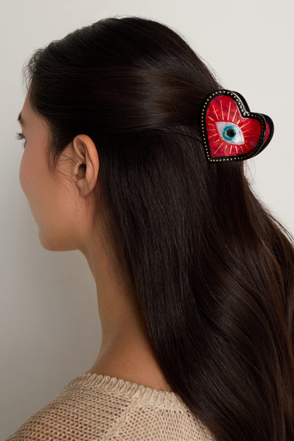 A woman with long dark hair wears the Hand Painted Heart Hair Clip, featuring a blue eye design on a red heart-shaped background.