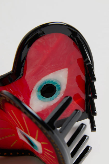 The Hand Painted Heart Hair Clip is a glossy red heart with a blue and white eye design, made from biodegradable cellulose acetate and shown close-up against a plain background.