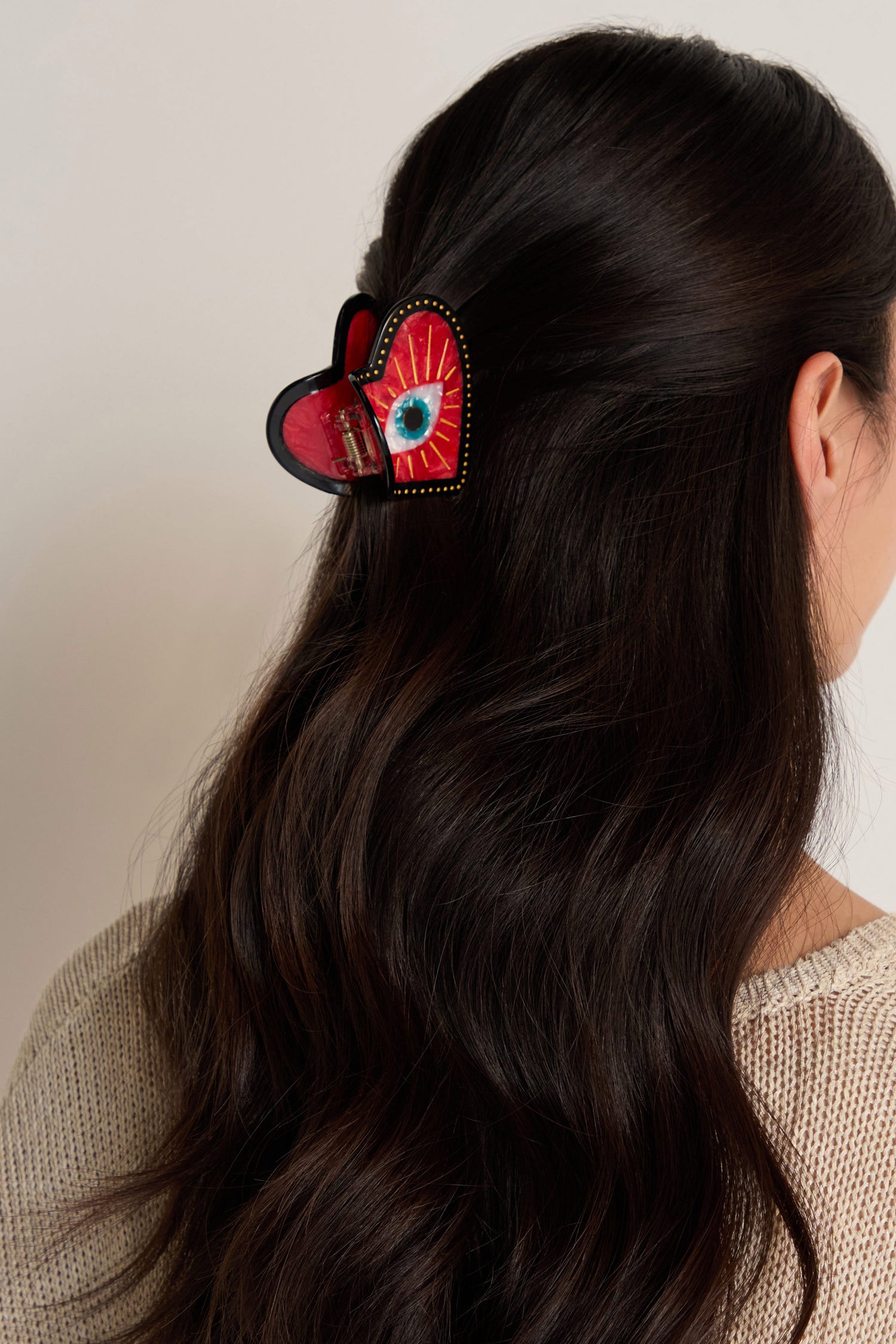 A woman with long dark hair wears the Hand Painted Heart Hair Clip, featuring an eye design on biodegradable cellulose acetate, at the back of her head.