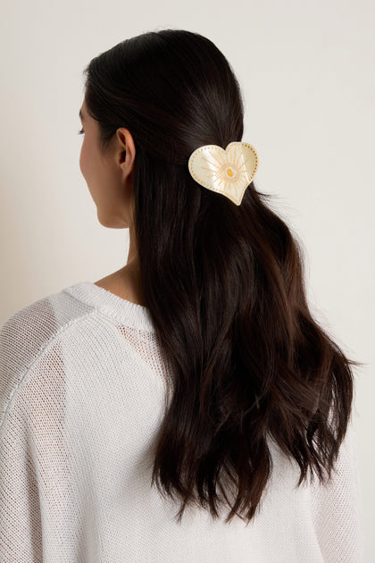 A woman with long, dark wavy hair, seen from behind, wears a Hand Painted Celestial Heart Hair Clip in cream with gold detailing.