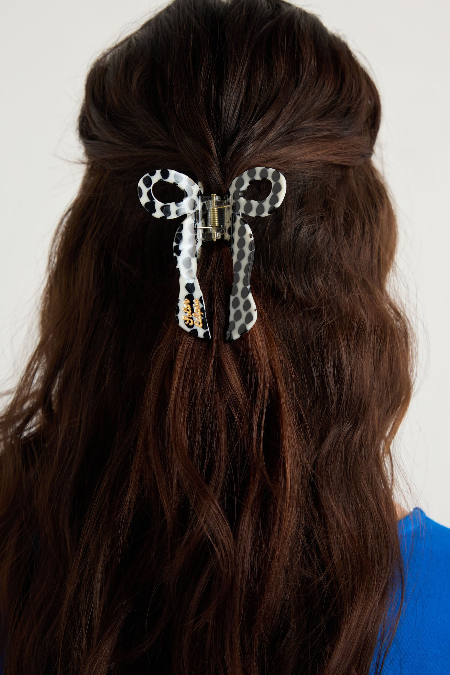 A person with wavy brown hair uses the Hand-Painted Coquette Bow Hair Clip, a clear cellulose acetate clip shaped like a polka-dotted bow, to secure the top half of their hair.