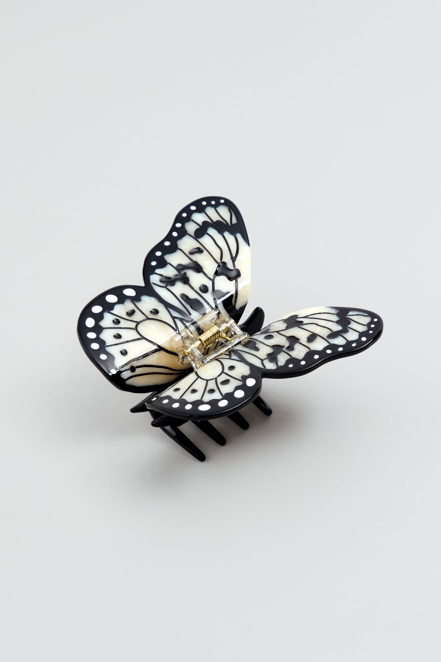 The Hand-Painted Kite Butterfly Hair Clip, featuring a black and white design and metal spring, is shown on a light gray background.