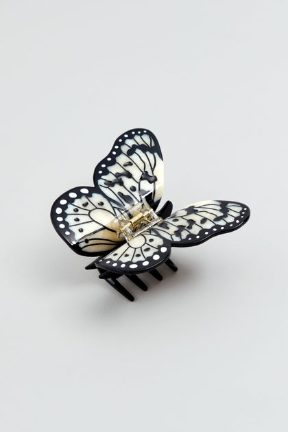 The Hand-Painted Kite Butterfly Hair Clip, featuring a black and white design and metal spring, is shown on a light gray background.