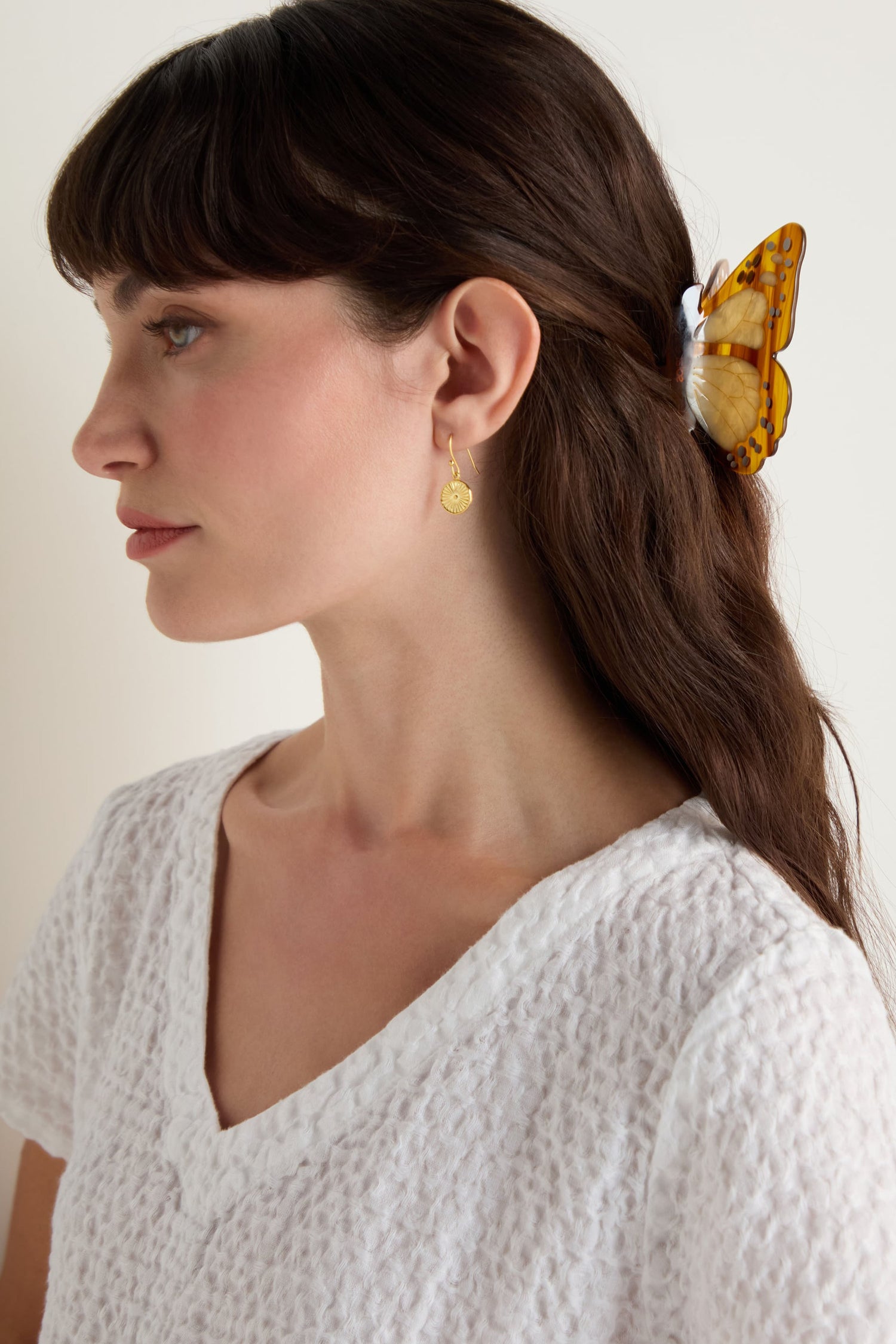 Woman with long brown hair and a small gold earring wears the Hand-painted Monarch Butterfly Hair Clip with a white textured top, shown in side profile against a plain background.