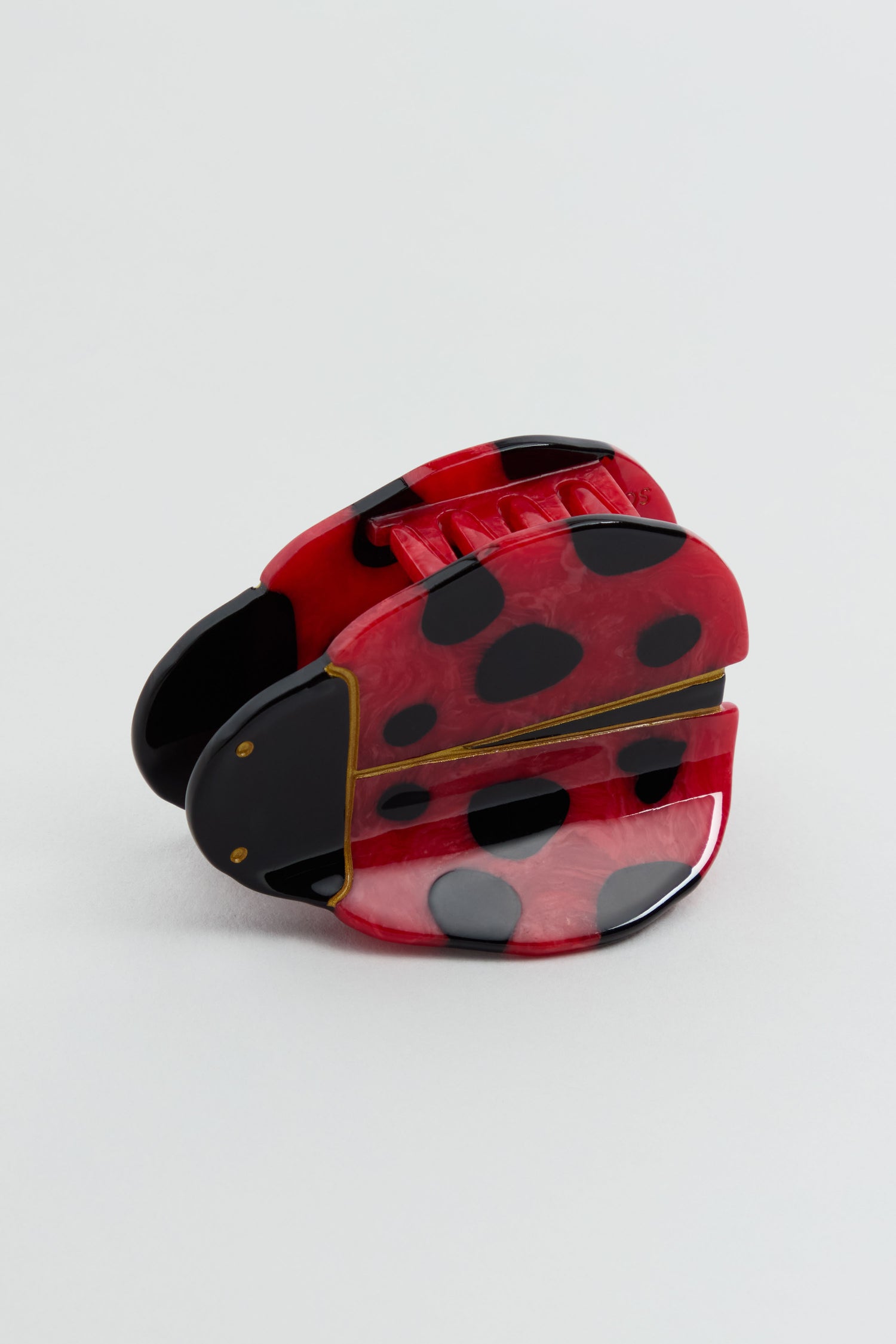The Hand-Painted Ladybird Hair Clip, featuring red and black spots on glossy plastic, is shown as a charming accessory against a neutral background.