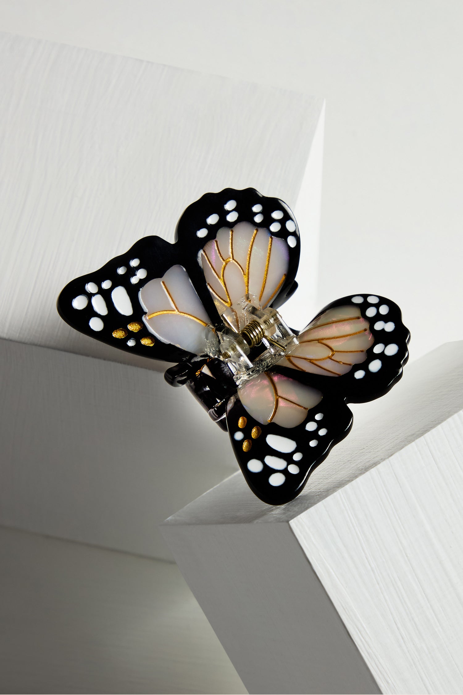 The Hand Painted Mini Monarch Hair Clip showcases butterfly-shaped black and white wings with gold accents. Made from biodegradable acetate, it is elegantly set on a white geometric base, perfect for elevating any outfit.