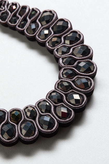 Close-up of the Velvet Ribbon Statement Necklace, featuring dark faceted oval stones set in paired loops on a light background.