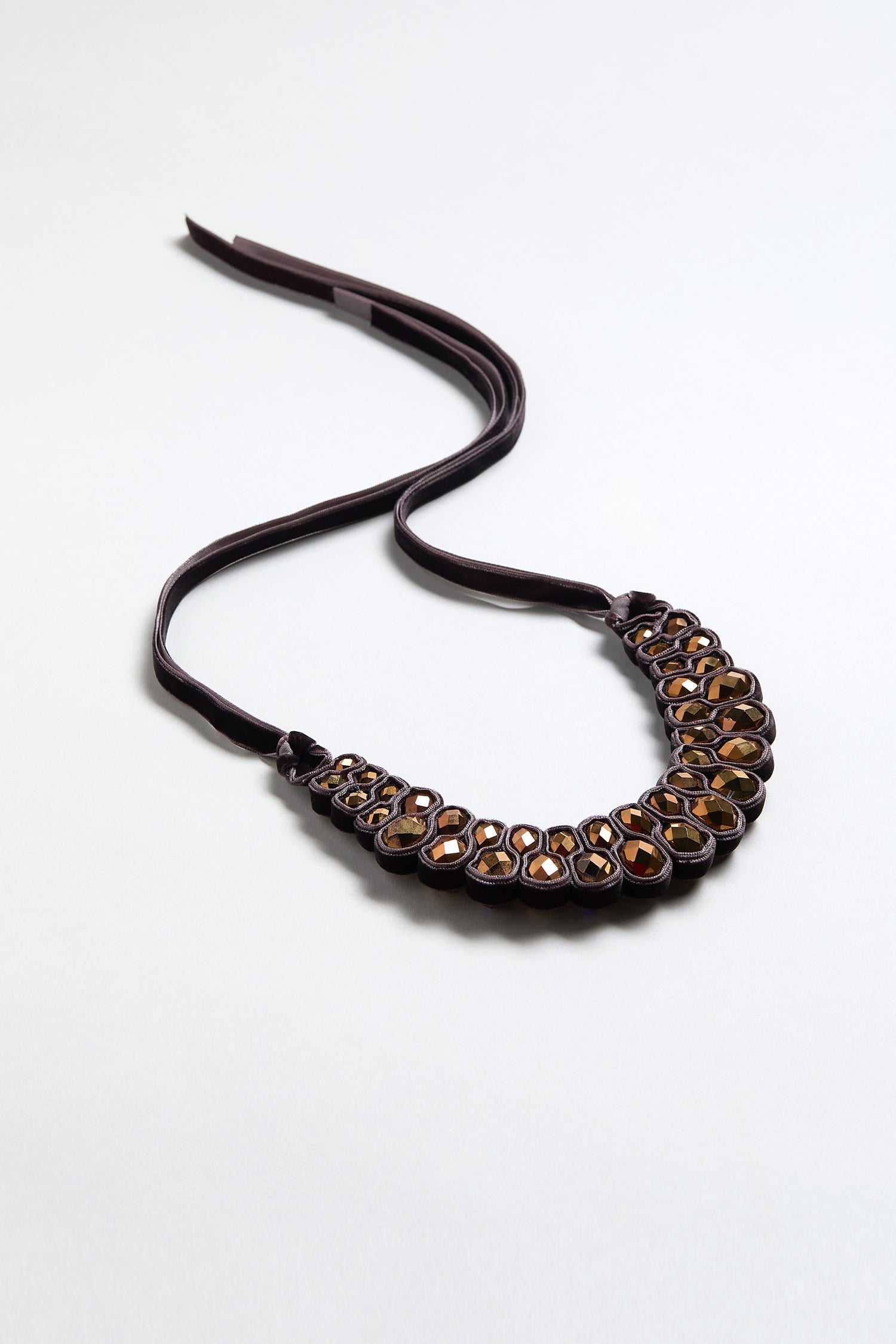 The Velvet Ribbon Statement Necklace features dark leather with multiple oval and round amber-colored stones in raised bezels, shown against a light background.