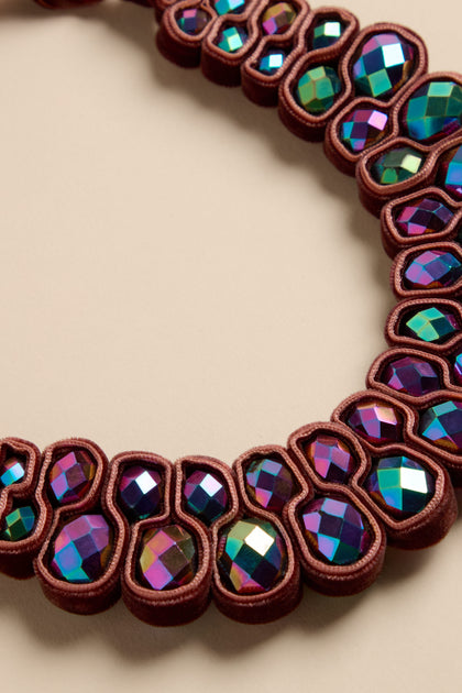 A Velvet Ribbon Statement Necklace featuring a semi-circular design with rows of iridescent crystals encased in dark brown ribbon.