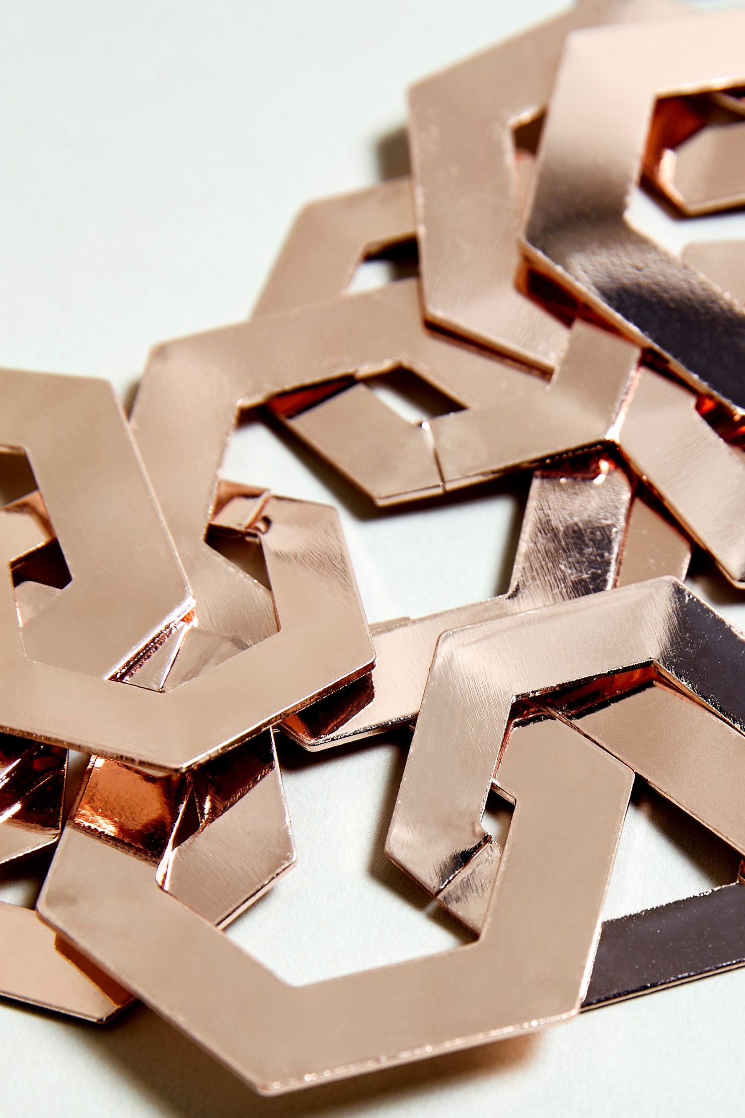 Close-up of interlocking, shiny rose gold hexagonal links on a neutral background highlights the modern design of the Hexagon Links Necklace.