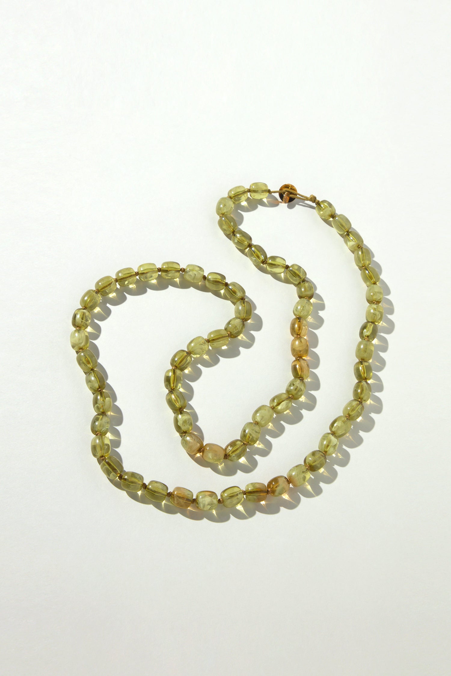 The Long Resin Bead Necklace is a versatile accessory featuring translucent oval yellow beads in a single strand, exuding subtle earthy khaki tones against a plain white backdrop.