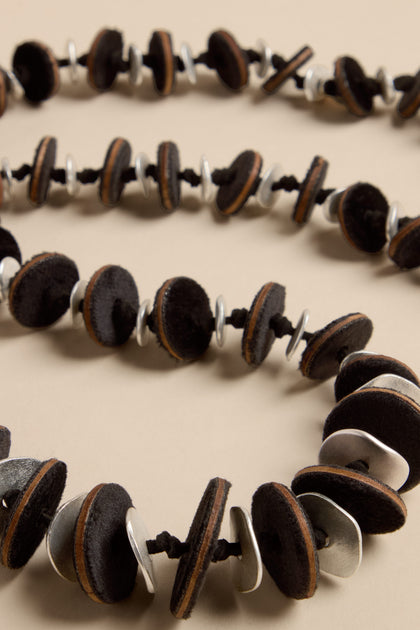 Velvet Detail Disc Necklace consisting of a long strand of alternating black velvet discs and silver-tone metal rings threaded onto a black cord.