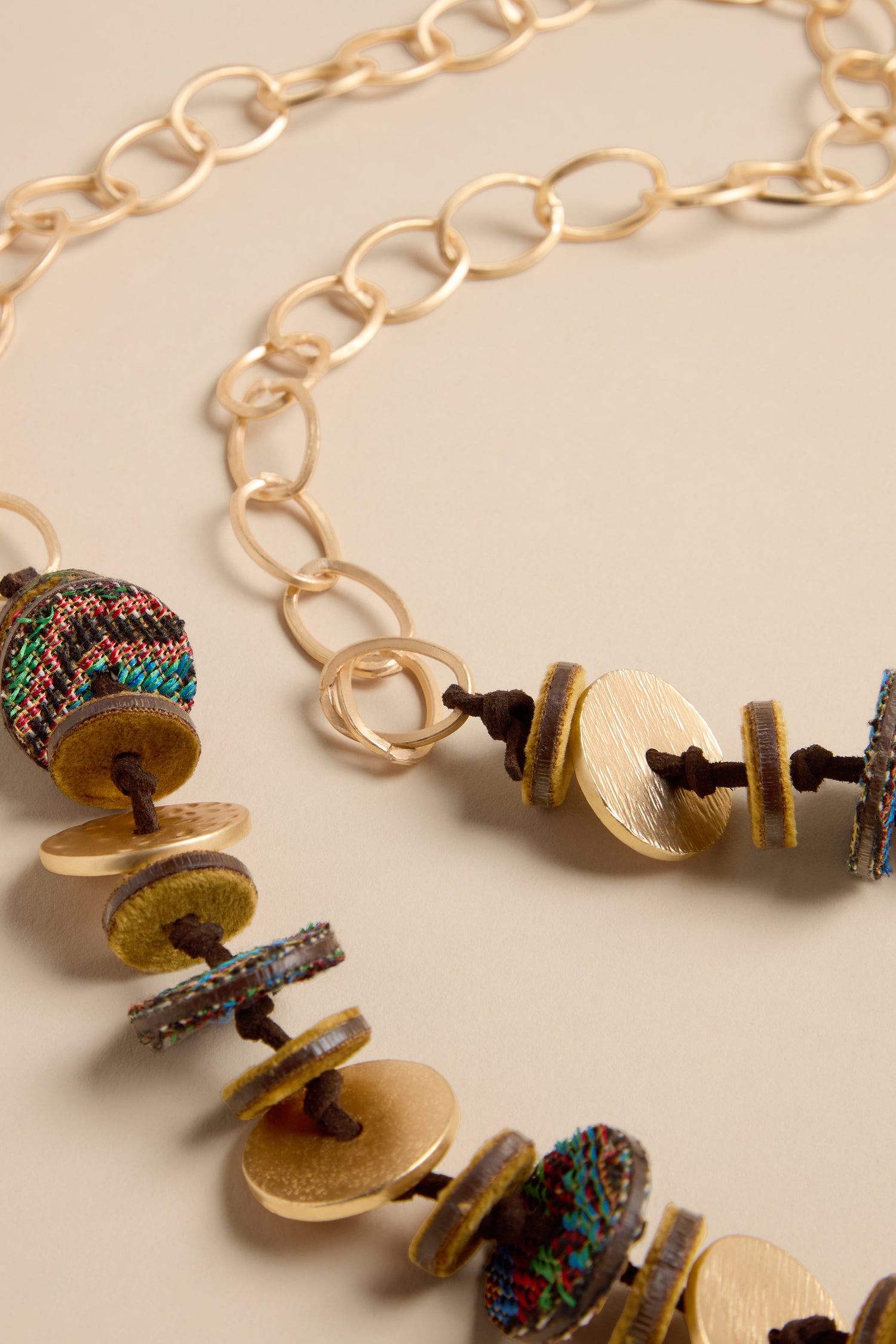 Textured Disc Necklace featuring gold-tone chain links, alternating metal discs, and colorful woven fabric circles on a brown cord.