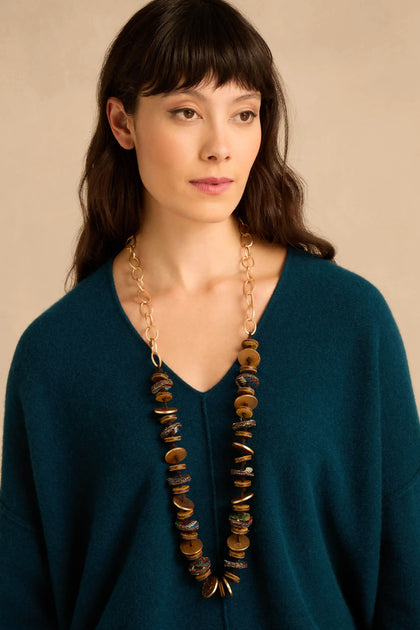 A person wearing a Textured Disc Necklace featuring a long gold-link chain with multiple stacked, textured disc pendants in brown and metallic tones.