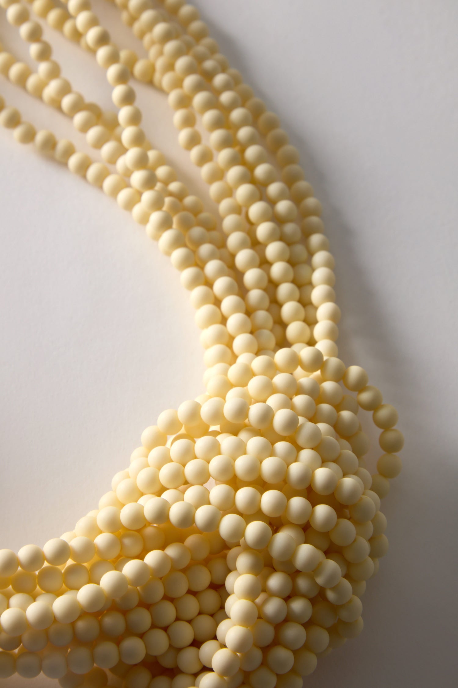 Close-up of the Knotted Bead Necklace displays multiple strands of cream round beads, artfully laid on a plain white surface, exuding artisanal charm.