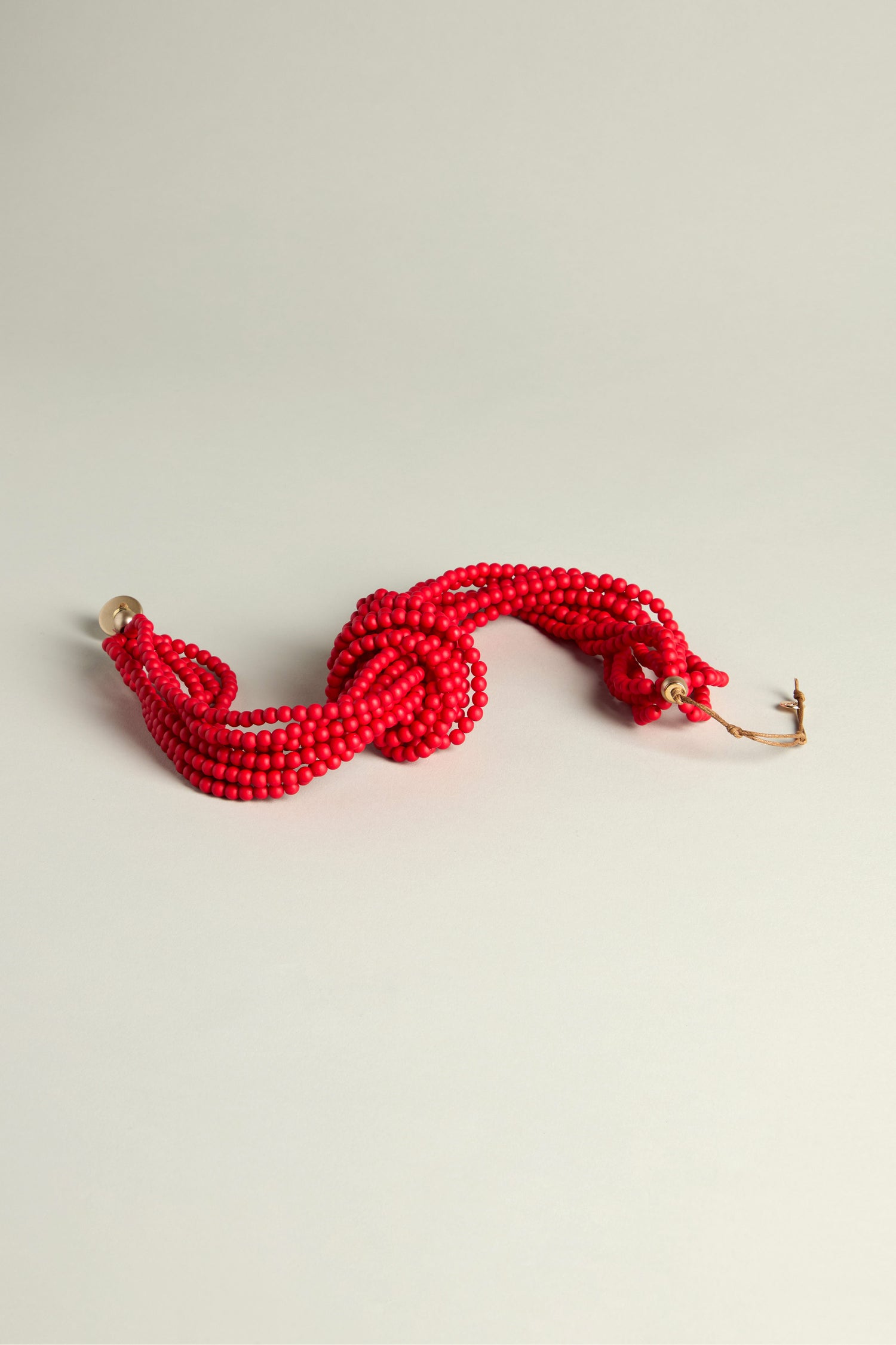 The Knotted Bead Necklace, adorned with striking red beads twisted into an attractive statement piece, is beautifully displayed on a light surface.