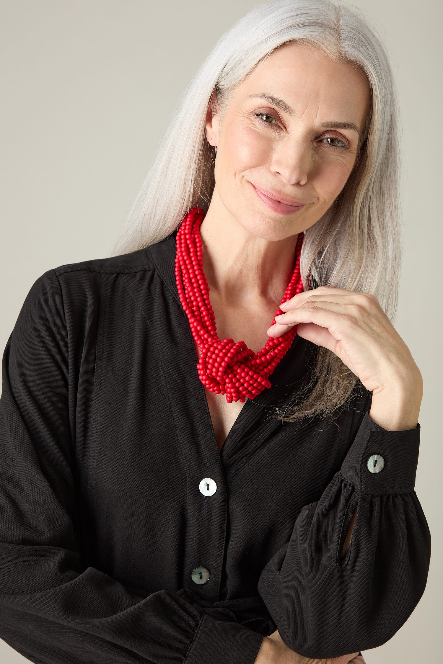 A person with long gray hair wearing a black button-up shirt and the vibrant Knotted Bead Necklace smiles at the camera, showcasing this statement piece beautifully.