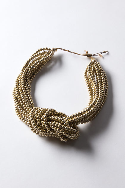 The Gold Knotted Bead Necklace features a central knot design with golden-toned beads, elegantly displayed on a plain surface.