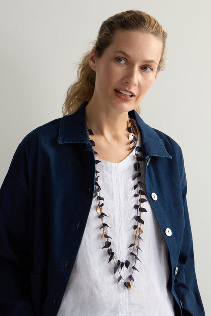 A person wearing a blue jacket over a white shirt and a Navy Cascade Leaves Necklace with gold-toned details stands in front of a plain background.